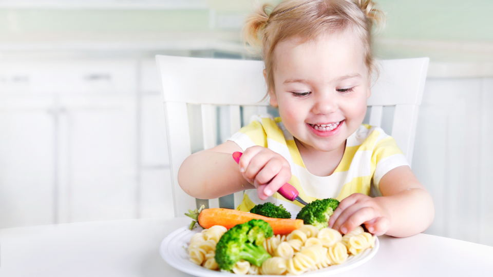 child with plate of food containing vegetables and pasta